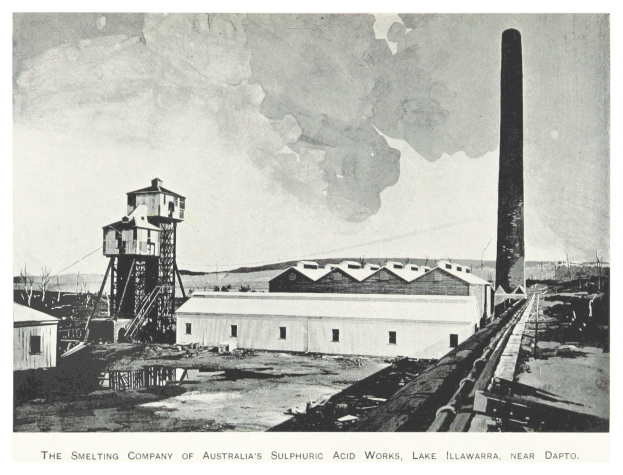 Schwarzes und weißes Foto einer Industrieanlage mit mehreren Gebäuden, einem hohen Turm und Rauch, der aus einem Schornstein aufsteigt, mit Text am unteren Rand.