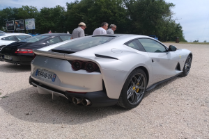 Roter Ferrari 812 Superfast auf dem Goodwood Festival of Speed mit Leuten in Kappen, Bäumen, Texttafeln und bewölktem Himmel im Hintergrund.