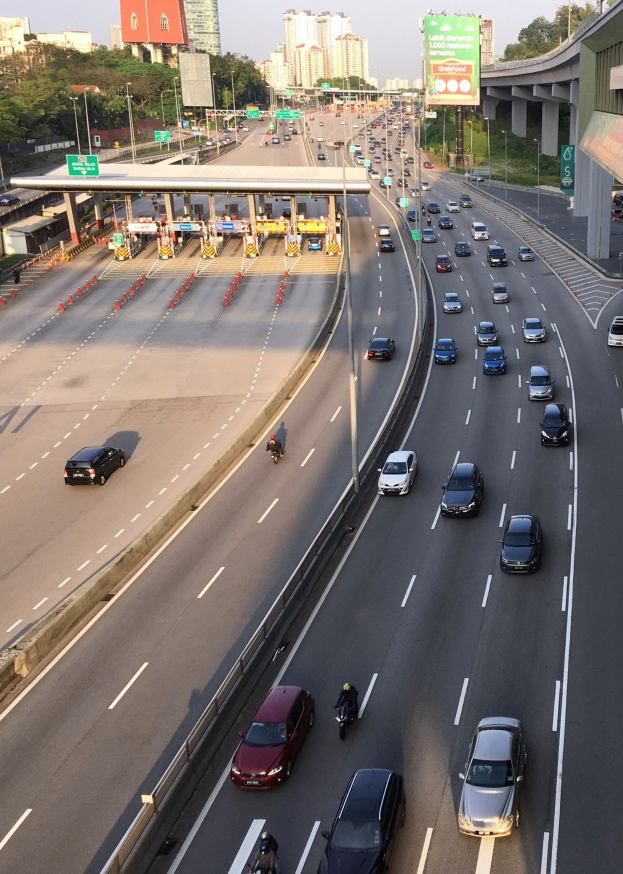 Eine belebte Autobahn mit Autos, Motorrädern, Verkehrskegeln, Straßenschildern, Laternen, einer Brücke, Bäumen, Gebäuden und einem klaren blauen Himmel.