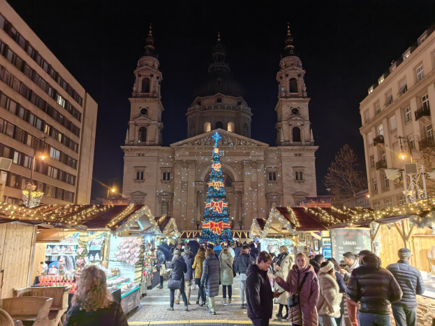 Weihnachtsmarkt mit festlichen Ständen, Lichtern und Menschen vor einer Kirche bei Nacht unter einem sternenklaren Himmel.