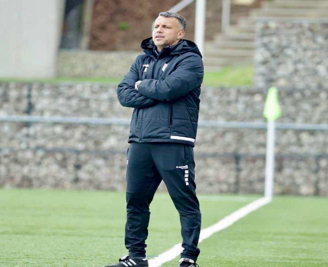 Ein Mann in schwarzer Jacke und Hose steht auf einem Fussballfeld mit überkreuzten Armen, scheinbar ein Trainer in einer Trainingseinheit.