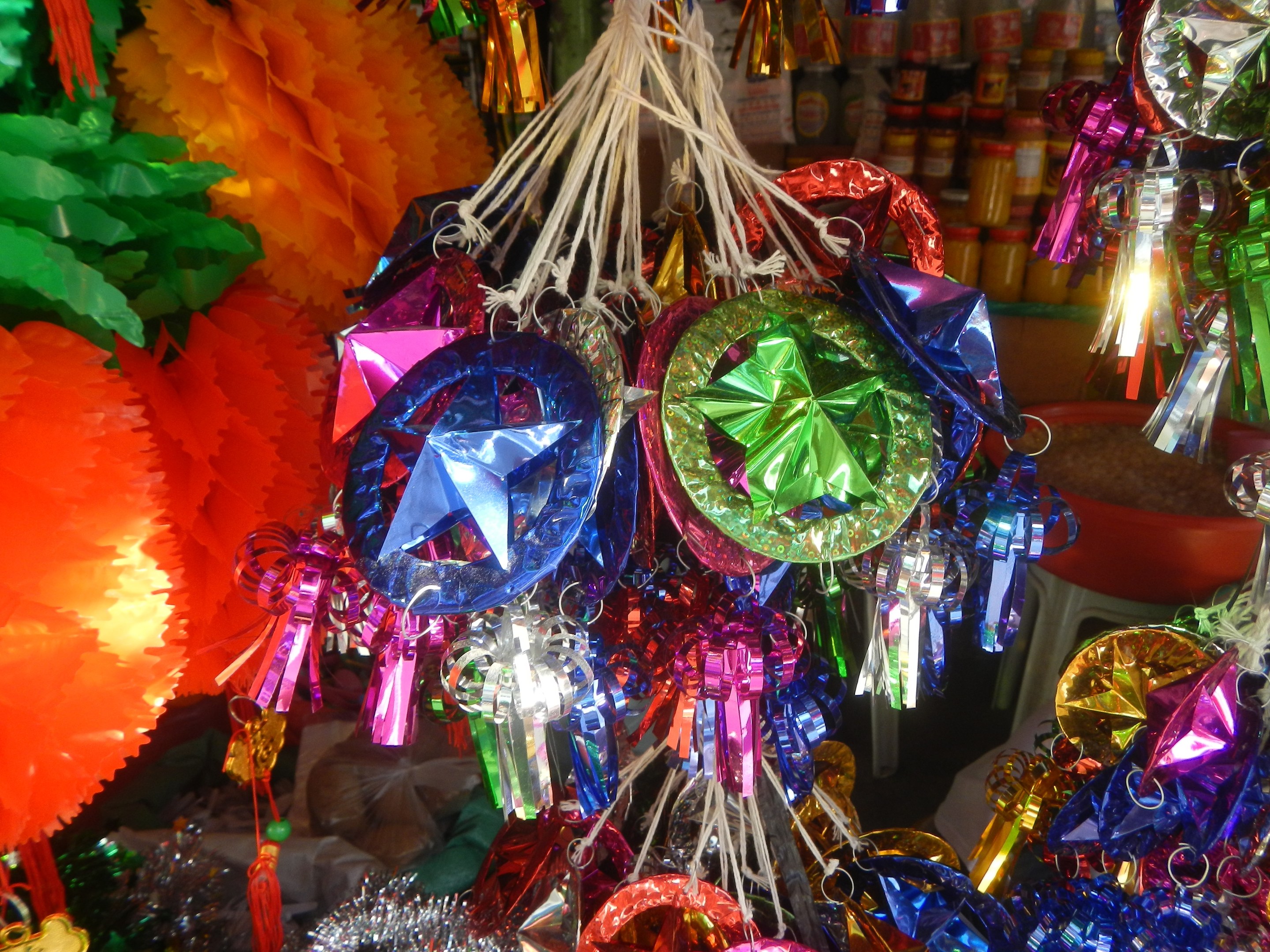 Bunte Dekorationen wie Laternen und B├Âgen h├Ąngen von der Decke über Regalen mit Flaschen in einer festlichen Atmosph├Ąre.