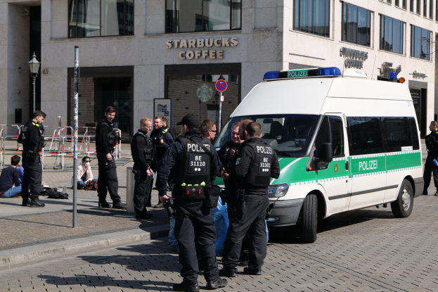 Eine Gruppe von Polizeibeamten vor einem Starbucks-Café, mit einem Van rechts und einigen Menschen links, vor einem Hintergrund mit Fenstern, einem Schild, einem Laternenpfahl und einem Zaun.