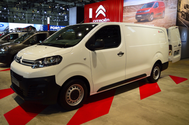 Ein weißer Citroen Berlingo Van wird auf einer Autauschau präsentiert, umgeben von schwarzer Schlafzimmer-Möbel, mit Wänden, die mit Brettern und Lichtern verziert sind.