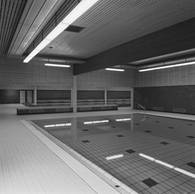 Innenbad mit klarem Wasser, gefliesten Wänden und Boden, Deckenleuchten und minimaler Umgebung in einem große, friedlichen Gebäude.