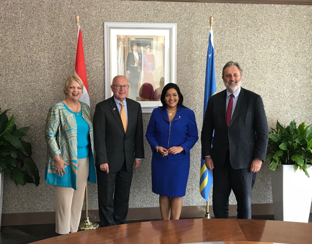 Eine Gruppe strahlender Menschen um einen Tisch mit Papieren versammelt, umgeben von Fahnen, Topfpflanzen und einem Fotorahmen an der Wand, feiert die Unterzeichnung eines Memorandums von Verständnis zwischen den Vereinigten Staaten und Kanada.