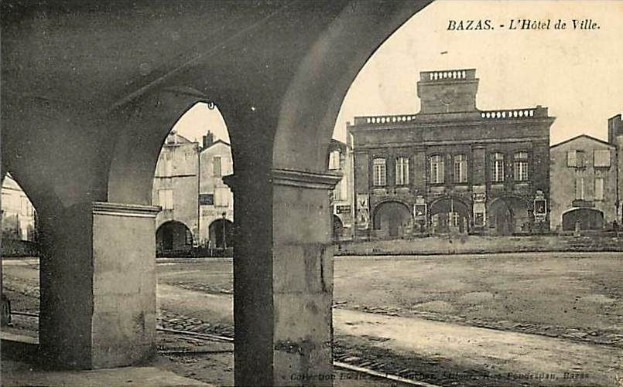 Schwarz-weiß-Foto einer Stadtstraße mit Gebäuden, Bögen, einer Bahnschiene und dem Text "bazas - l'hotel de ville" oben und unten.