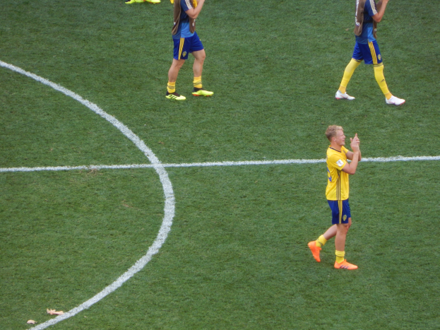 Mannengruppe in Fußballtrikots klatscht feiernd auf einem Fußballfeld.