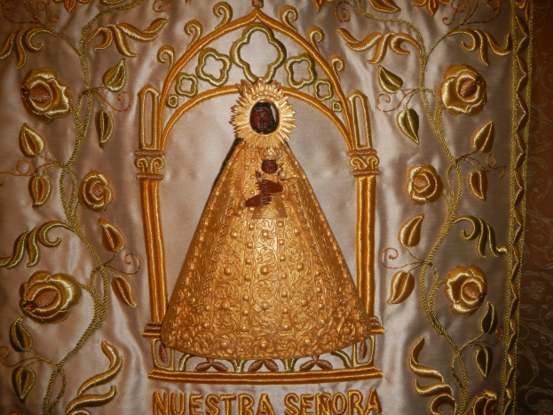 Goldbestickter Chasuble mit einer friedlichen Frau in einem hochgeschlossenen, langärmeligen Kleid mit einem Dutt, umgeben von detaillierten Texten und prächtigen goldenen Designs.
