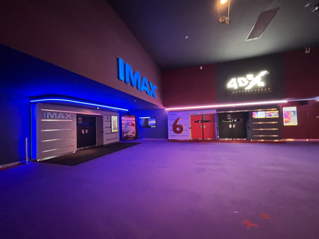 Innenansicht eines Kinos mit einem violetten Teppich, Text und Bildschirmen an den Wänden und Deckenbeleuchtung.