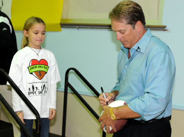 Mann in blauem Hemd und schwarzen Hosen, der einen Fussball für ein Mädchen in weißem T-Shirt unterschreibt, das einen Stift in der anderen Hand hält.