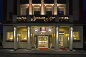 Das Essenerhof Hotel in Berlin, Deutschland, ein mehrstöckiges Gebäude mit Fenstern, Türen, Säulen, Lampen und einem Namensschild, mit einer Straße und Fahrzeugen auf der rechten Seite.