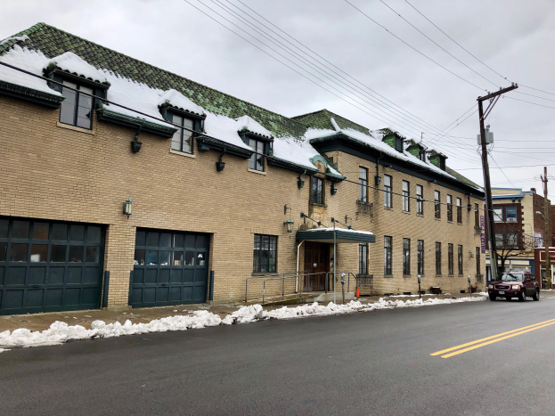 Großes Backsteingebäude mit einem grünen Dach an einer Straßenkreuzung, umgeben von Fahrzeugen, Schnee, Strommasten, Bäumen und einem bewölkten Himmel, identifiziert als die ehemalige Feuerwache St. Louis.