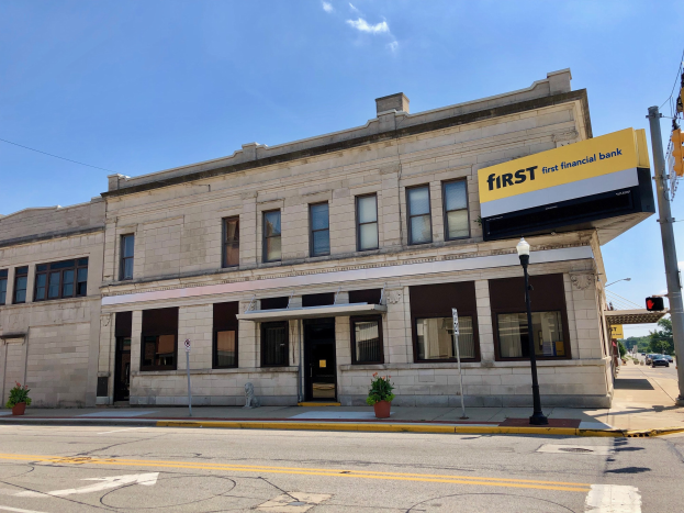 Großes Gebäude mit einem "First Financial Bank"-Schild, umgeben von Straßeninfrastruktur, Fahrzeugen, Vegetation und einem bewölkten Himmel.