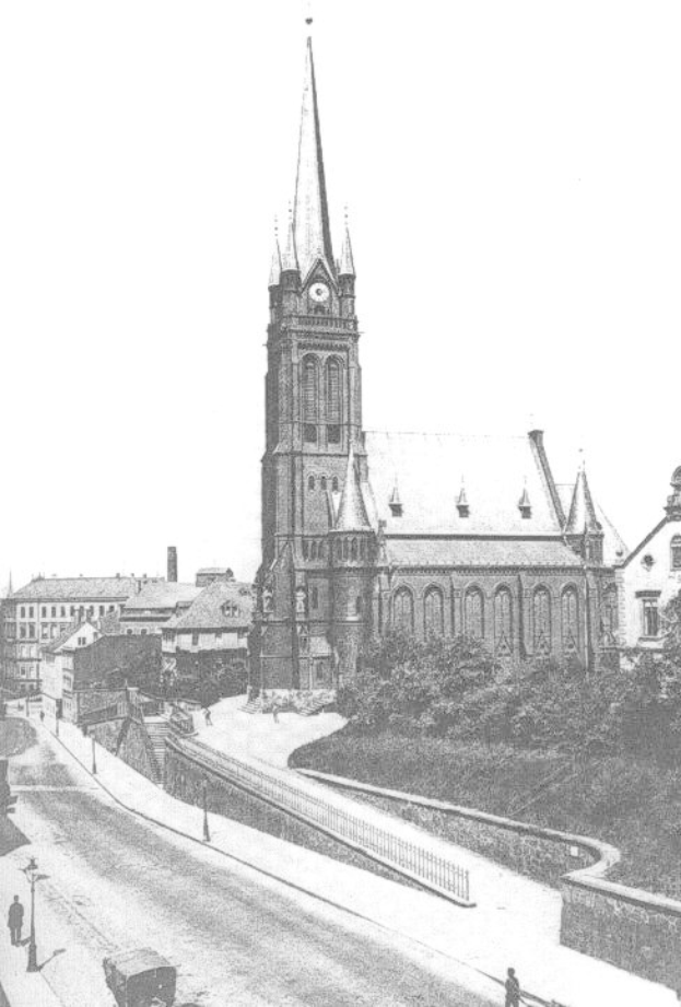 Schwarzes und weißes Foto einer Stadtstraße mit St. Peter Kirche im Hintergrund, Wiesbaden, Deutschland, gesäumt von Gebäuden, Bäumen, Fahrzeugen und Passanten.
