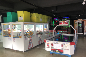 Ein Raum voller verschiedener Arcade-Spiele, mit einem Spielautomaten auf der rechten Seite, einem sichtbaren Boden und Deckenlampen.