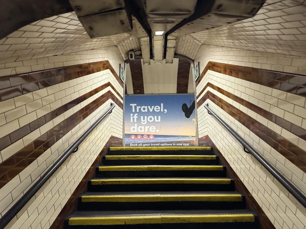 Eine Treppe in einer U-Bahn-Station mit einem 'Reise, wenn du wagst'-Schild oben, flankiert von Geländern und U-Bahn-Stationswänden im Hintergrund.