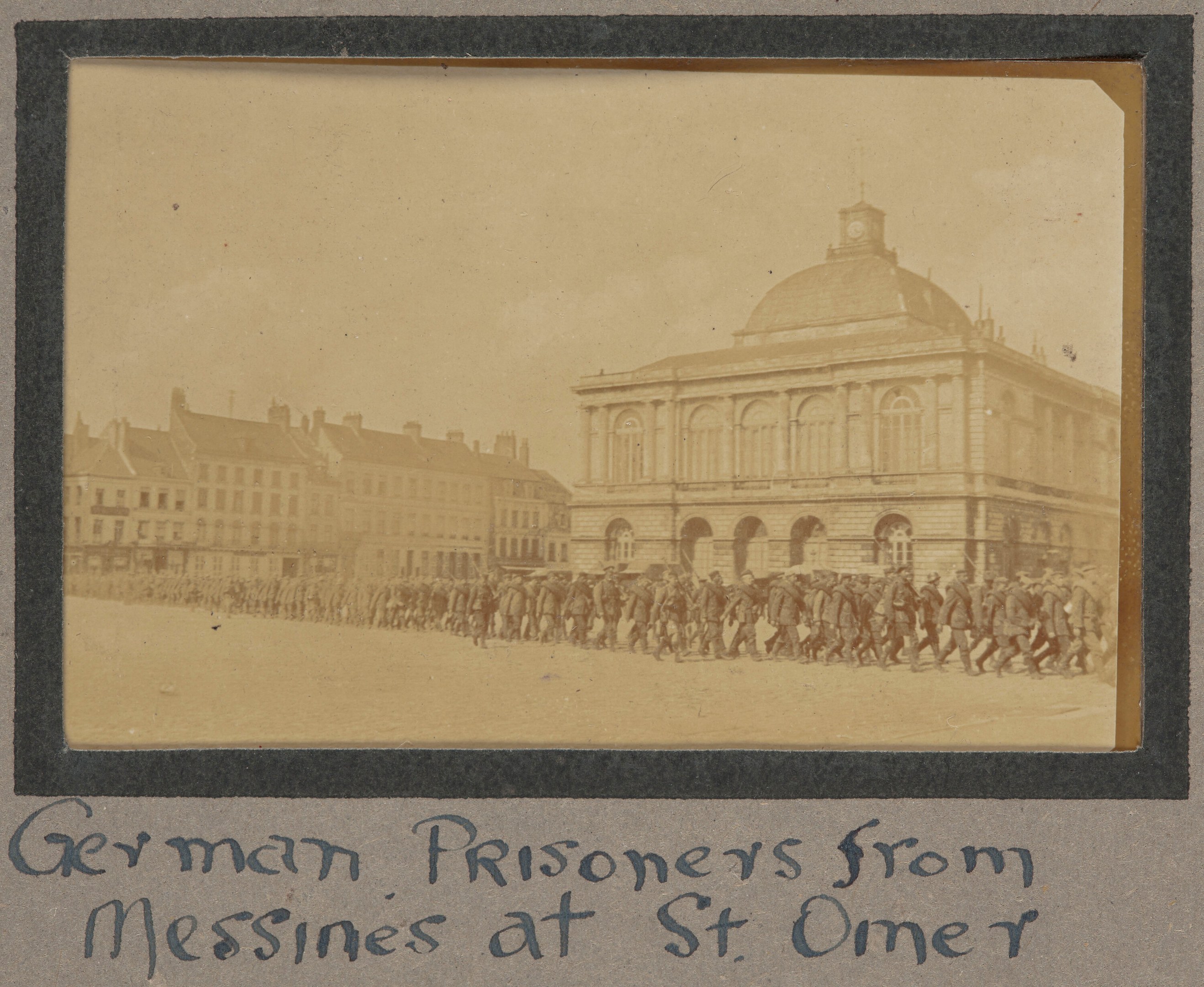 Gruppe deutscher Gefangener aus Messines vor einem Gebäude mit klarem blauen Himmel im Hintergrund, mit Text unten.