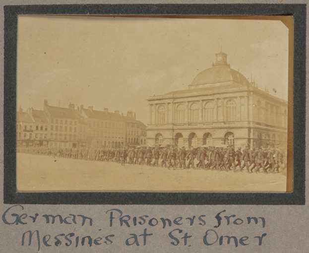 Gruppe deutscher Gefangener aus Messines vor einem Gebäude mit klarem blauen Himmel im Hintergrund, mit Text unten.