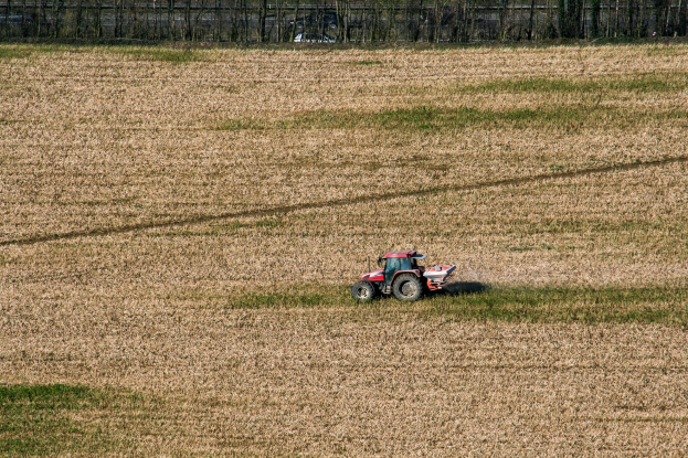 Eine Person fährt einen Traktor auf einem Feld, mit Gras und Bäumen im Hintergrund.