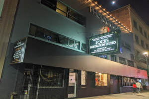 Außenansicht des Focus Innovation Studio in New York City bei Nacht, mit beleuchteten Fenstern und Namensschildern an umliegenden Gebäuden, Menschen auf dem Gehweg und sichtbarem Nachthimmel.