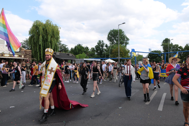 Eine Gruppe von Menschen, die bei der Gay Pride Parade 2018 marschieren und eine Regenbogenflagge sowie Musikinstrumente tragen.