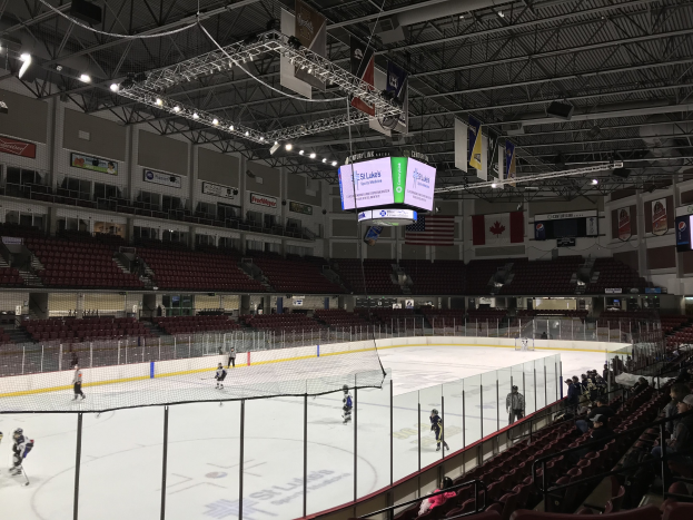 Eishockeyspiel in einer großen Arena mit einem zentralen Netz, Zuschauern auf beiden Seiten, Deckenbeleuchtung und Bannern, als St. Louis Blues Arena identifiziert.