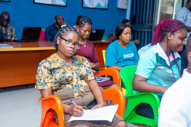 Eine Gruppe von Menschen sitzt in einem Raum mit Laptops, Büchern und anderen Gegenständen auf Tischen während einer Veranstaltung, die wie ein Seminar über Bildung in Ghana aussieht.