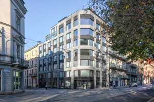 Großes Bürogebäude mit zahlreichen Fenstern, umgeben von Straßeninfrastruktur, Fahrzeugen, Fußgängern, Bäumen und einem bewölkten Himmel, das als neue Firmenzentrale dient.
