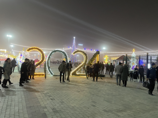 Menschen auf einer nächtlichen Straße, beleuchtet von Gebäuden und Laternen, einige mit Taschen unterwegs bei einer Silvesterfeier.