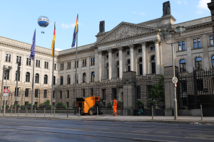 Großes modernes Gebäude mit vielen Fenstern, als Bundestag in Berlin, Deutschland identifiziert, umgeben von Straßeninfrastruktur, Fußgängern und Flaggen, unter einem bewölkten Himmel.