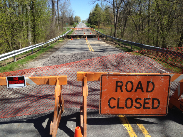 Verkehrsschild mit Absperrkegeln, einem Zaun, Gras, B├Ąumen und einem bew├Âlktem Himmel.