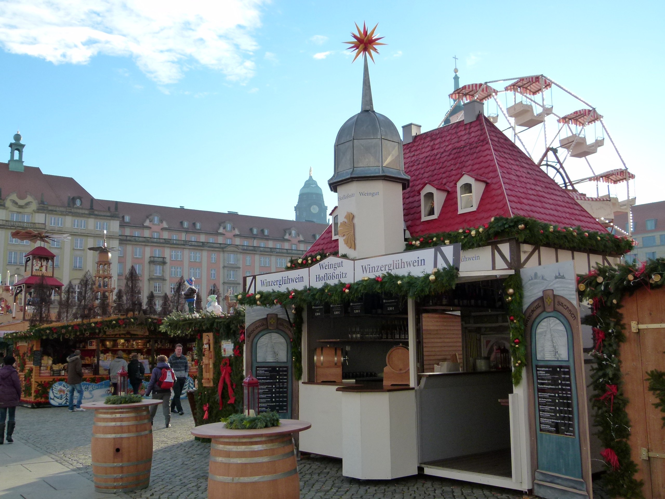 Ein geschäftiges Weihnachtsmarkt in Nürnberg, Deutschland mit Menschen um geschmückte Stände, festliche Lichter, ein Riesenrad, Gebäude und ein Schild an der rechten Seite.