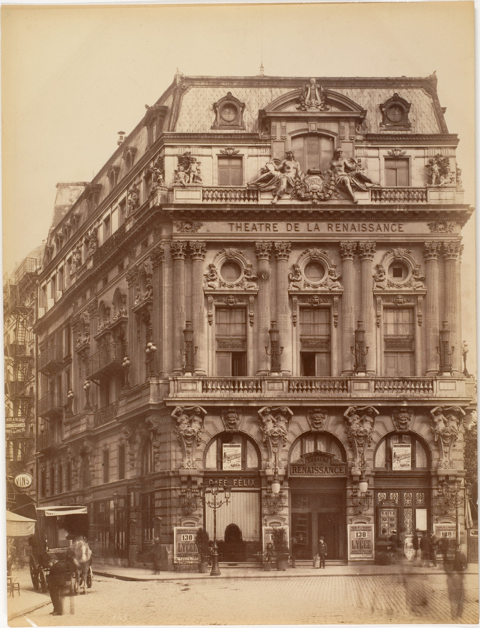 Schwarz-weiß-Fotografie des Théâtre de la Renaissance in Paris mit seiner Fassade, die Fenster, Säulen, Bögen und Skulpturen aufweist, sowie einigen Menschen und Fahrzeugen davor und dem Himmel im Hintergrund.