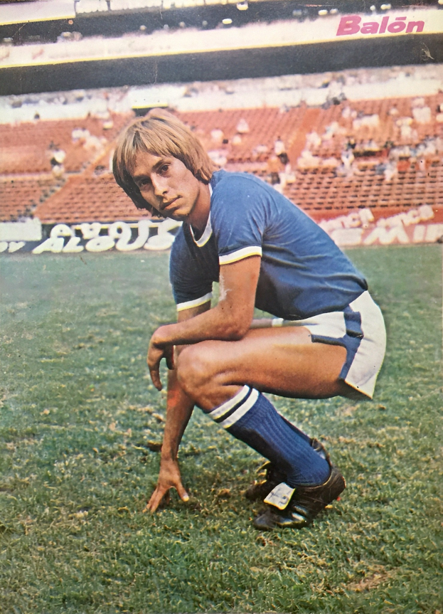 Ein Mann kniet auf einem Fuballfeld umgeben von Menschen, die auf Stühlen und Platten mit Text sitzen.