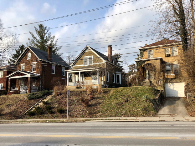 Reihe von Häusern mit Fenstern, Türen, Säulen, Geländern, Stufen, Pflanzen und Gras, entlang einer Straße mit Bäumen und einem Pfahl mit einem Schild, unter einem bewölkten Himmel, repräsentiert eines der teuersten Häuser zum Verkauf in Detroit.