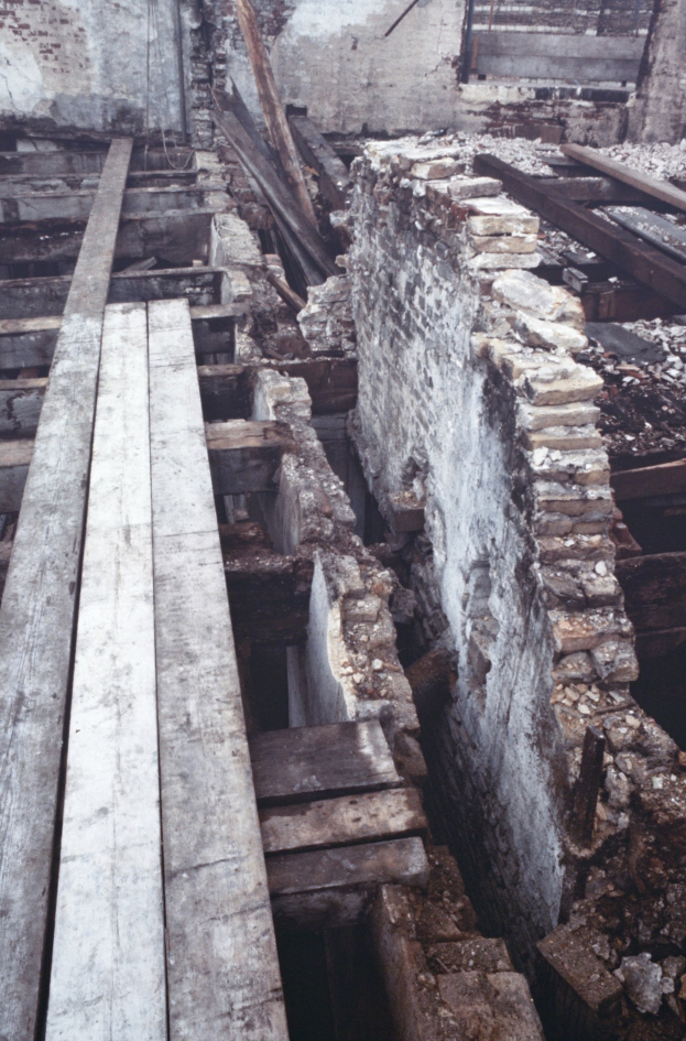 Altes Gebäude im Abriss mit verstreuten Holzplanken und Steinen im Vordergrund, Ziegelwand im Hintergrund.