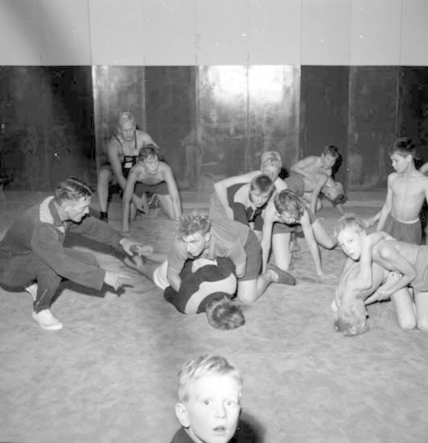Schwarz-weißes Foto von jungen Jungs, die in einer Turnhalle ringen, mit einer Wand im Hintergrund.