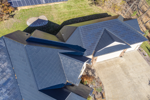 Luftaufnahme eines Hauses mit integrierten Solarmodulen auf dem Dach, umgeben von Bäumen, Gras und einem Zaun.