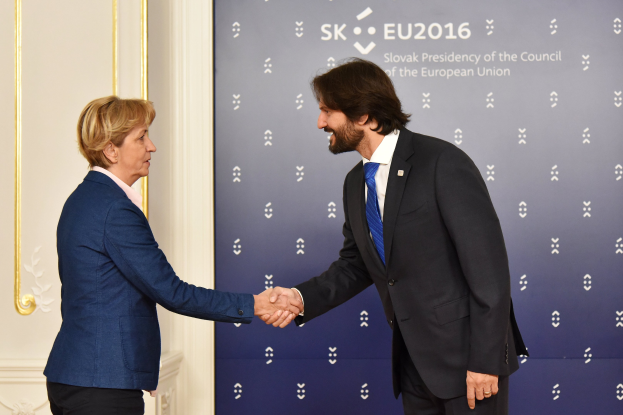 Bundeskanzlerin Angela Merkel und Bundespräsident Joachim Gauck geben sich die Hand vor einer Wand mit einem 'EU-Gipfel'-Schild und einer Tür im Hintergrund, beide lächeln.