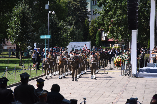 Eine Gruppe von Menschen mit Mönchen und Musikinstrumenten marschiert durch eine straßenlinke Allee, mit einem Podium und Mikrofon im Vordergrund und einer Zuschauermenge.