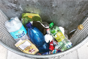Ein Metallmüllcontainer voller verschiedener Plastikflaschen, Tüten und anderer Gegenstände.