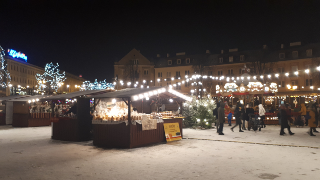 Weihnachtsmarkt bei Nacht mit Menschen, Buden und schneebedeckter Umgebung.