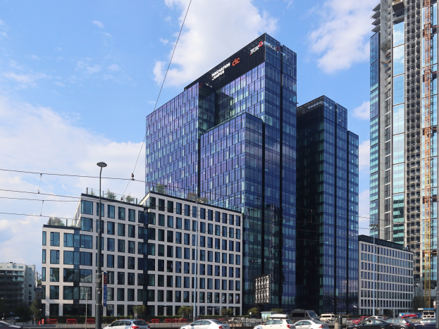 Zentrale der Deutschen Bank in Frankfurt, Deutschland, ein großes mehrfenstriges Gebäude umgeben von städtischer Infrastruktur und Grünfläche unter einem bewölkten Himmel.