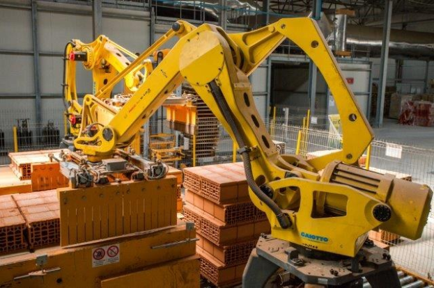 Großes Industrie-Lager mit gestapelten Kisten, Kränen, Zaun, Pfählen und einer fernen Wand in einer Fertigungseinrichtung.