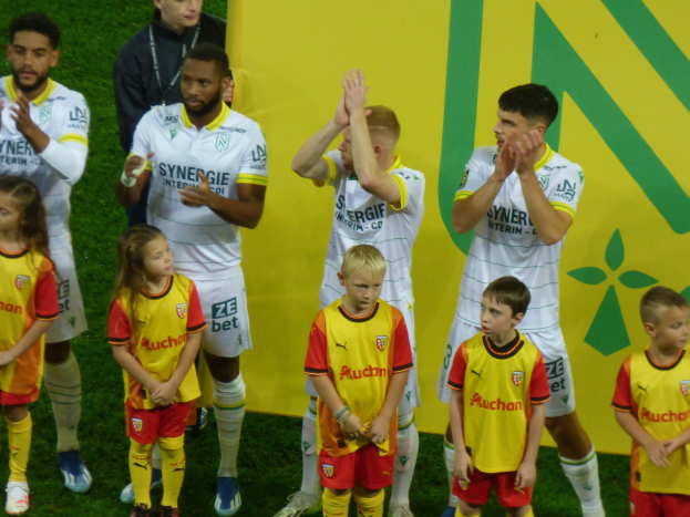 Eine Gruppe von Fussballspielern in Uniformen klatscht nach einem Sieg auf einem Ligue-1-Feld.