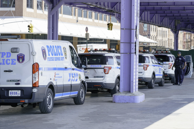 Polizeiautos entlang einer Stadtstraße geparkt mit einer Person auf der rechten Seite, Gebäude und eine Brücke im Hintergrund.