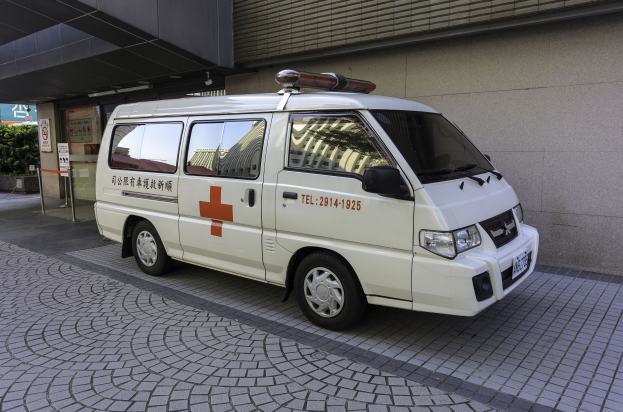 Ein Rettungswagen steht vor einem Gebäude mit einem Schild, umgeben von Bäumen und Pflanzen.