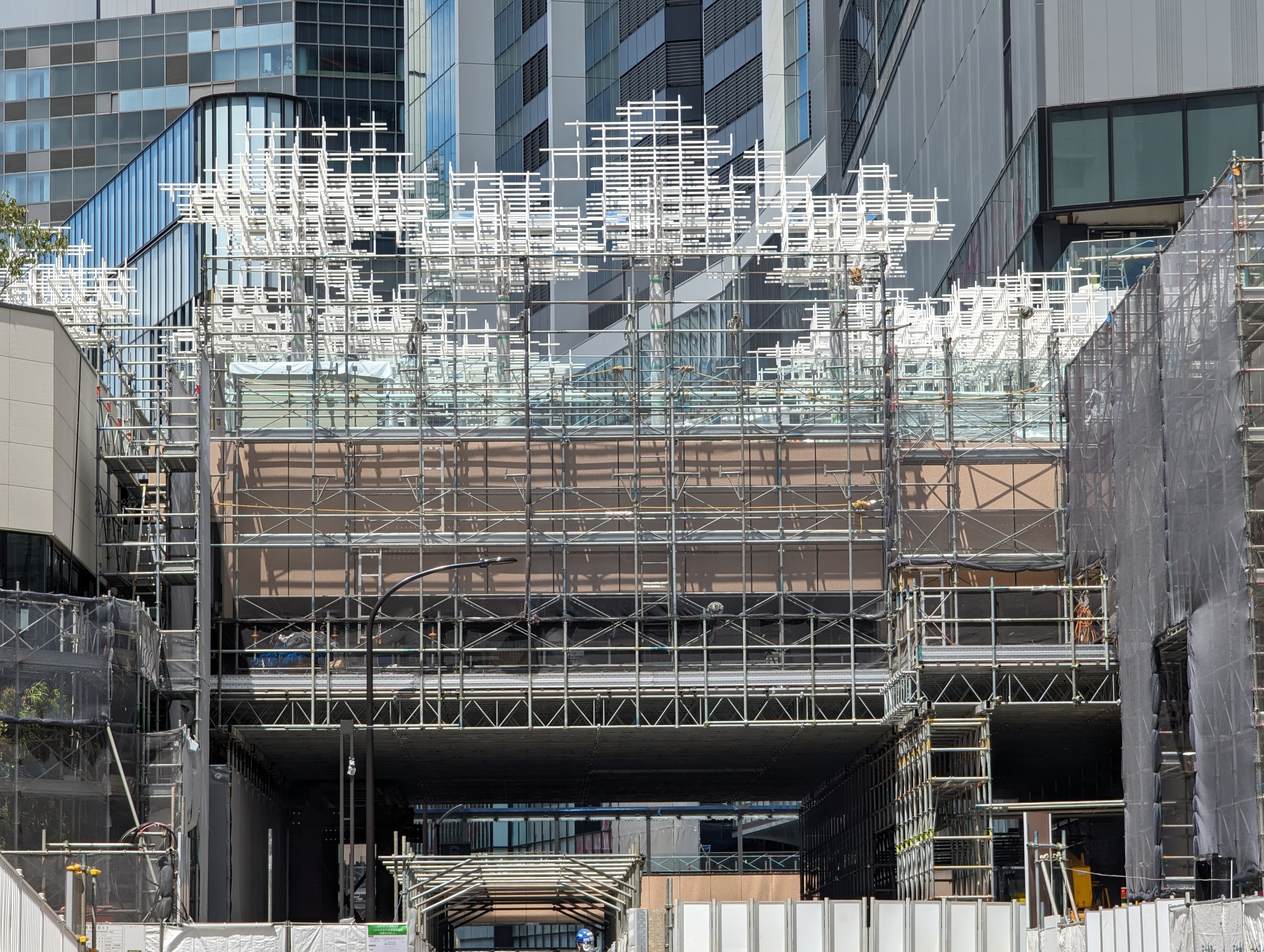 Großes Gebäude mit Gerüst, das renoviert wird, umgeben von Bäumen links und einer Straße unten.