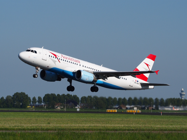 Airbus A320-200 der Austrian Airlines startet vom Frankfurter Flughafen, mit grünem Gras, Bäumen, Gebäuden und einer Kontrollturm im Hintergrund.
